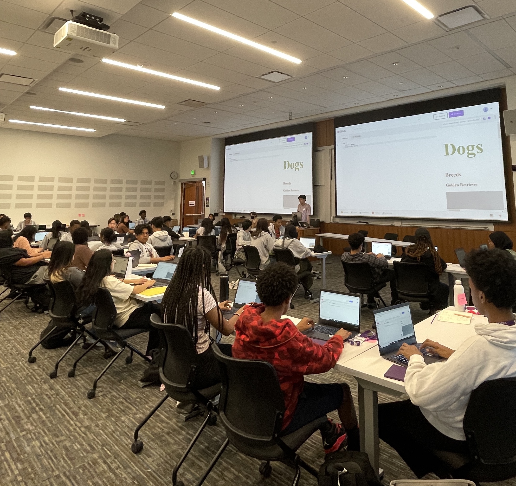 Students sitting in a classroom facing forward with laptops on their tables open