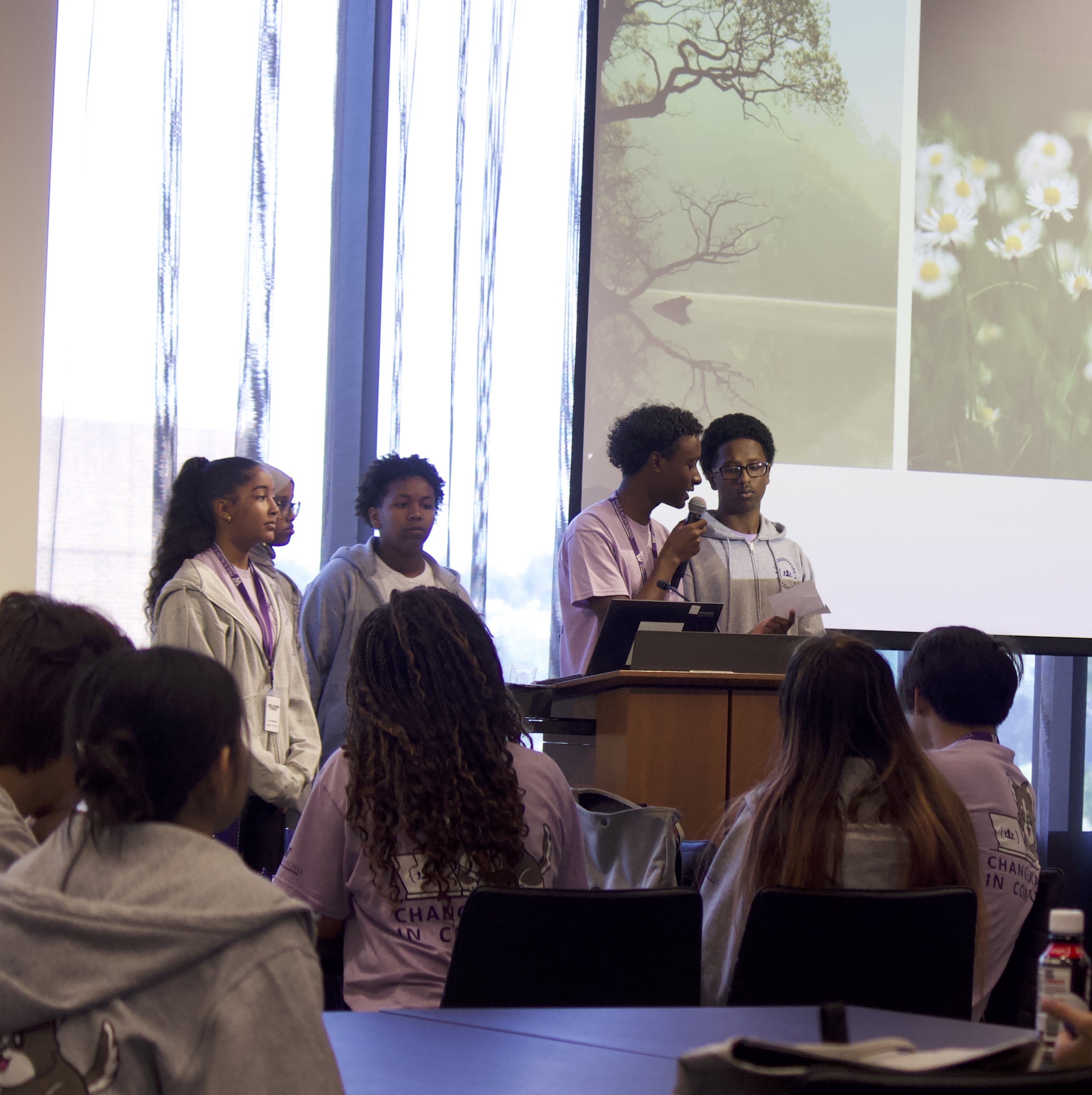 4 students presenting at a podium with an audience of sitting students